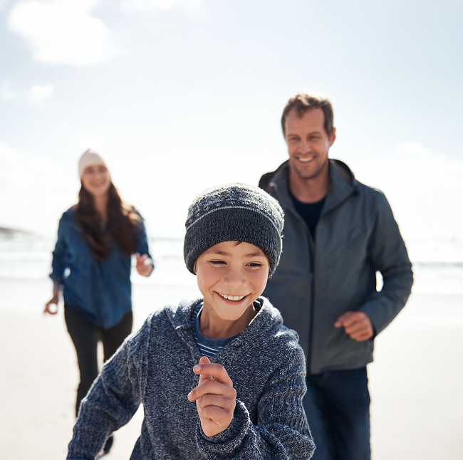 Child smiling and running on the beach with his mom and dad.